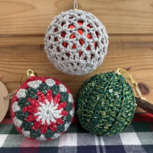 Each ornament features intricate crochet designs in classic Christmas colors, wrapped around a shimmering bauble